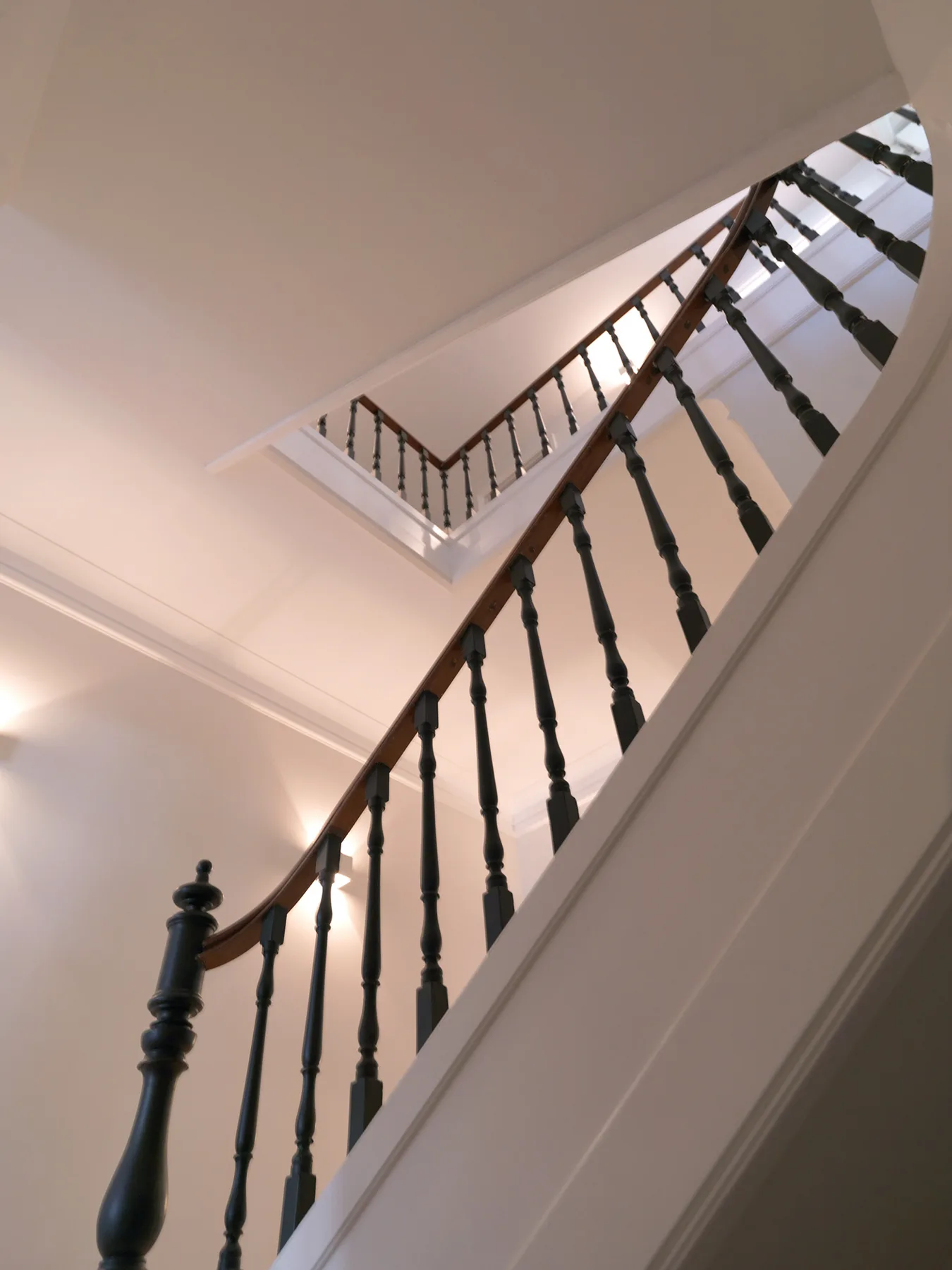 Una escalera interior con barandillas oscuras asciende por un hueco luminoso.