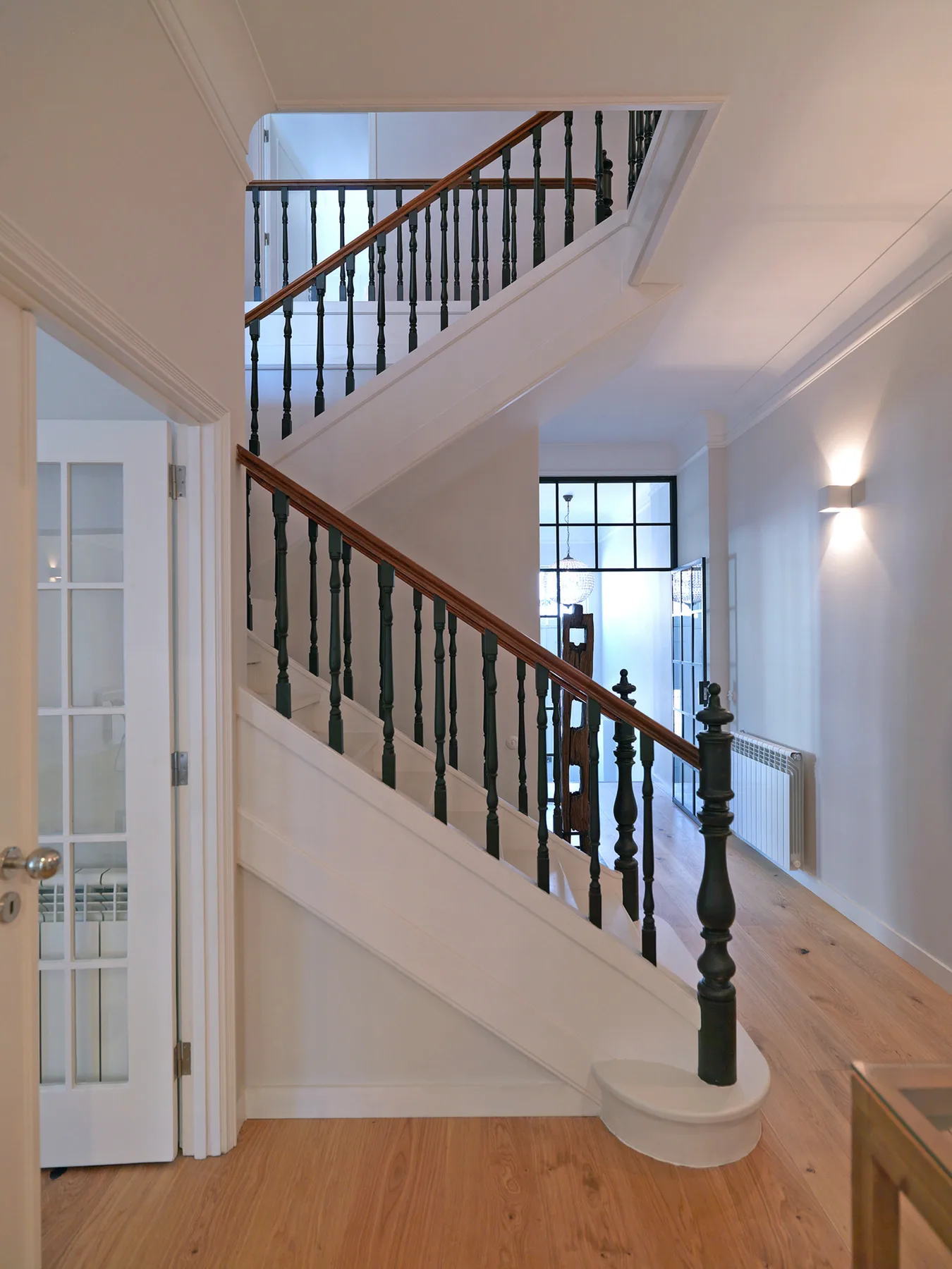 A bright stair hall with wooden steps and dark railings.