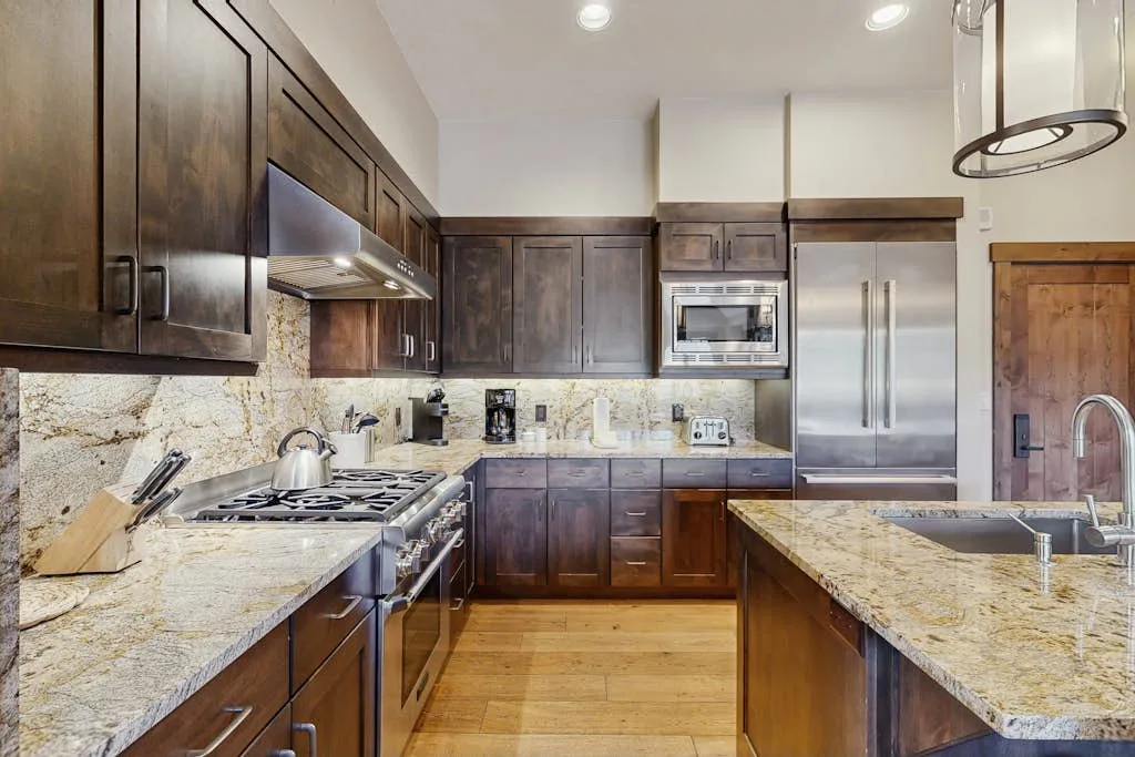 A spacious kitchen with dark cabinets, stone counters, and stainless steel appliances.