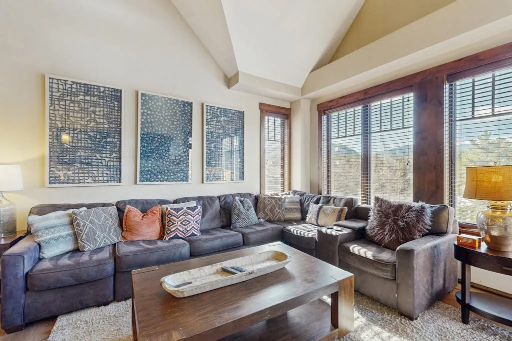 A living room with sectional seating, large windows, and a wooden coffee table.