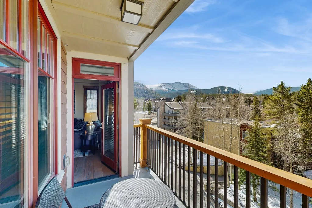 A balcony overlooks a wooded neighborhood and distant mountains.