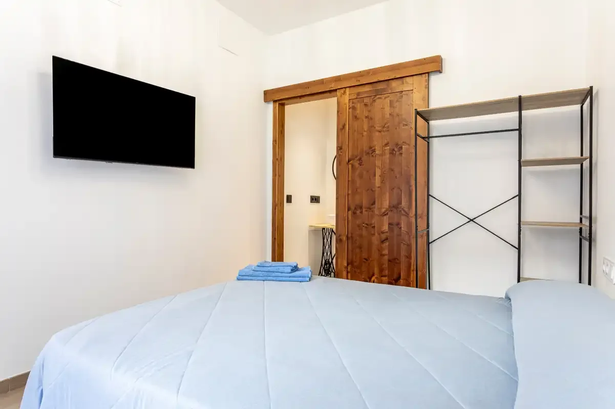A bedroom with light blue bedding, a wall-mounted television, and an open clothes rack.