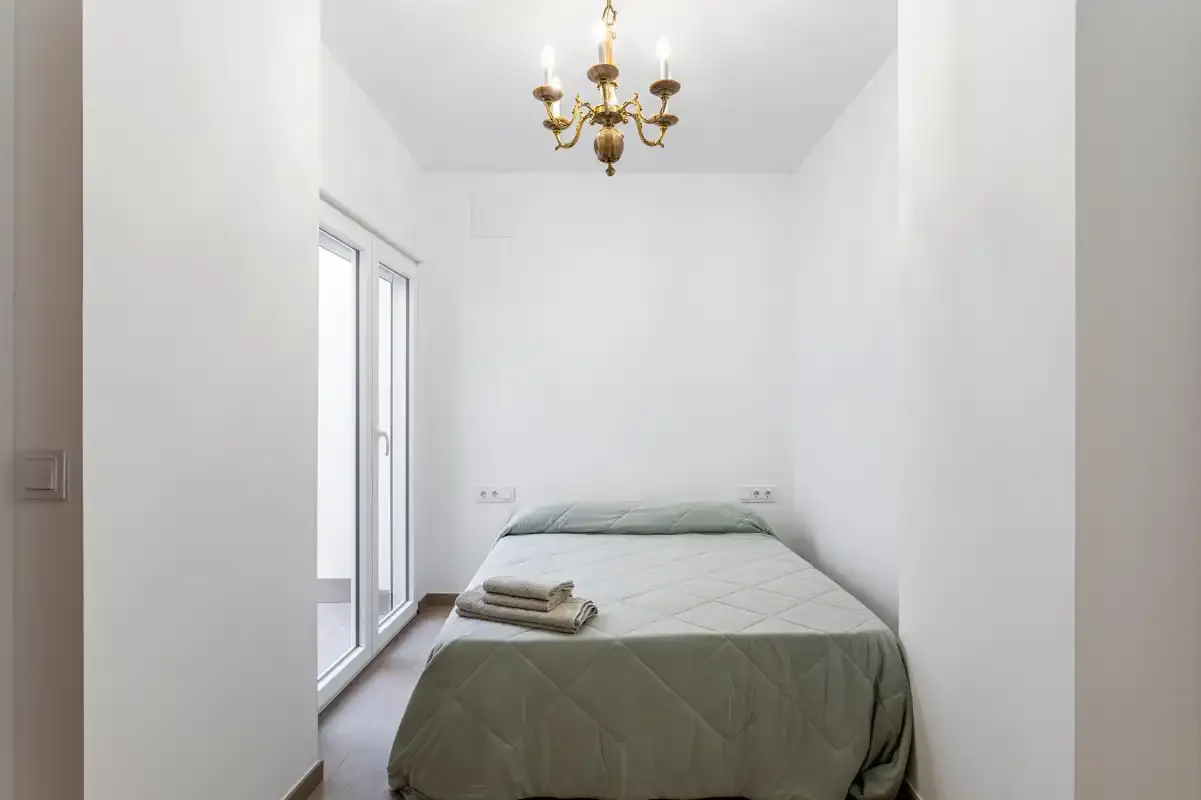 A bedroom with a bed beneath a chandelier and a glass door.