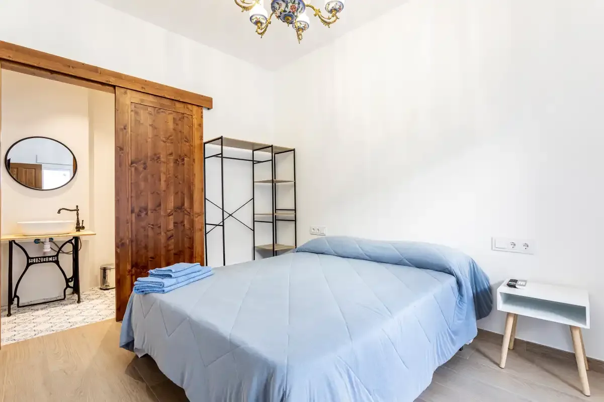 A bedroom with a bed dressed in blue bedding and a small bedside table.