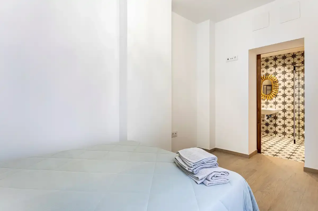 A bedroom with a bed and folded towels beside an open doorway.