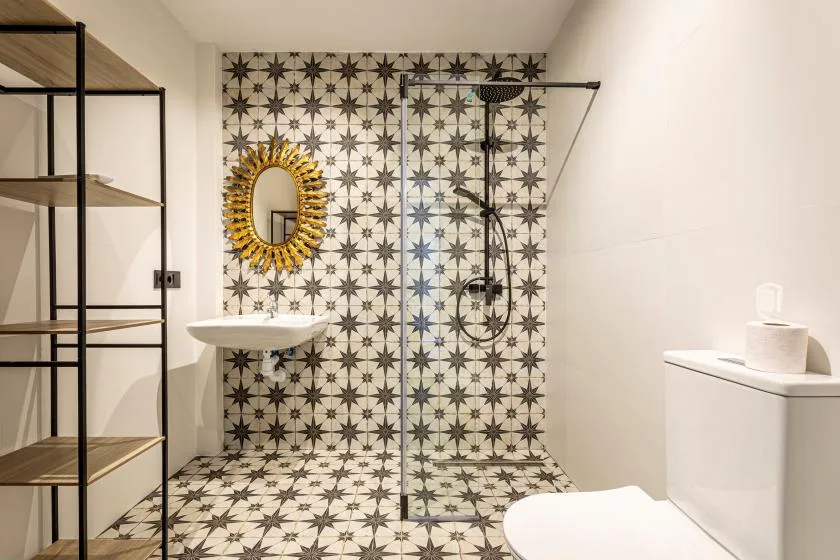 A bathroom with a patterned tile wall and a glass shower.