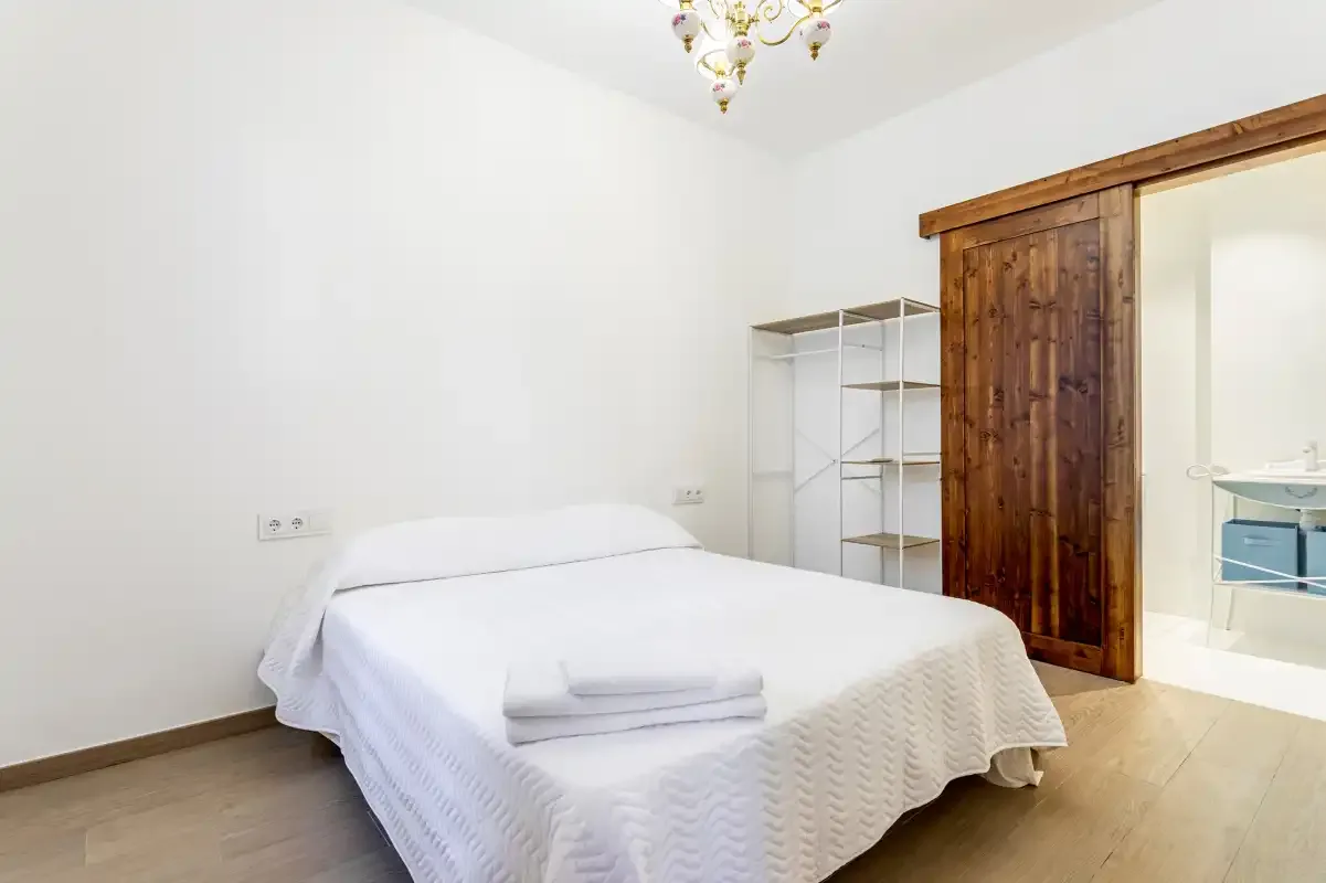 A bedroom with a bed and open shelving beside a wooden sliding door.