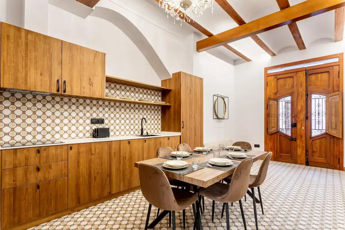 A dining area with a wooden table and a kitchen along the wall.