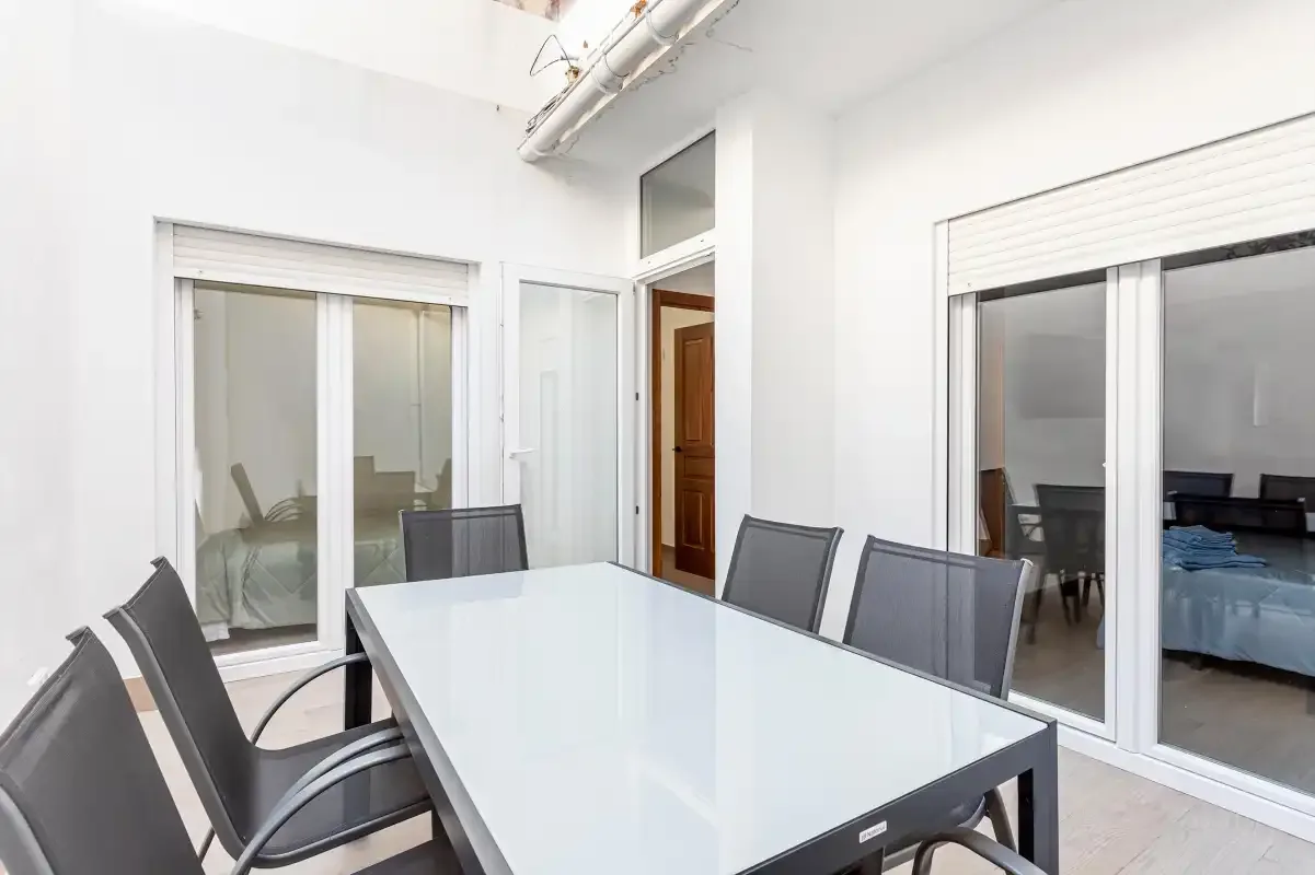A bright dining area with a long table and dark seating beside sliding glass doors.
