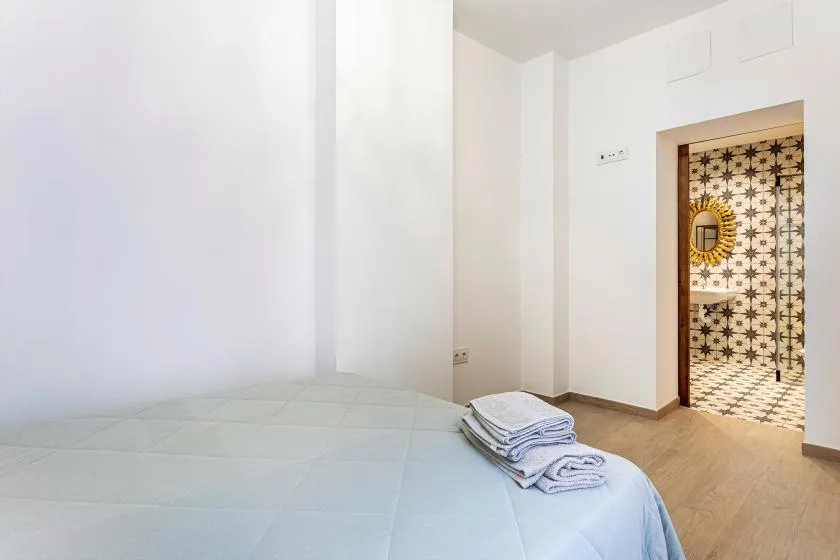 A bright bedroom with a bed beside an open doorway to a patterned room.