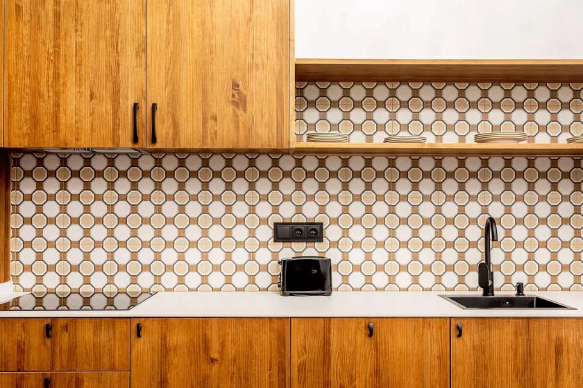 A kitchen counter with wooden cabinets, a patterned backsplash, and a sink.