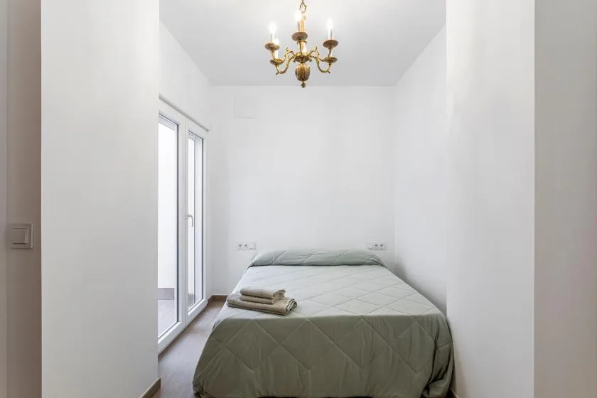 A bedroom with a bed, folded towels, and a chandelier.
