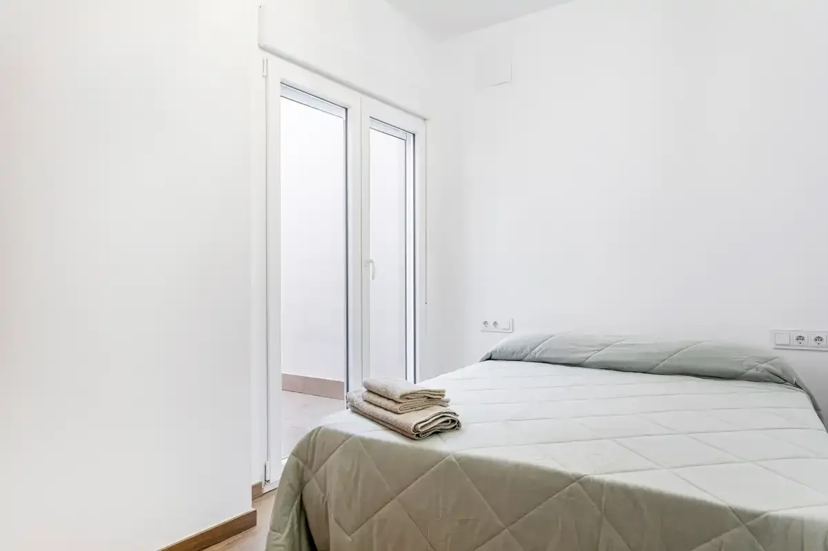 A bright bedroom with a neatly made bed and folded towels.