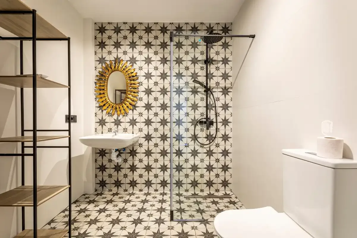 A bathroom with a patterned tiled wall and an open shower.