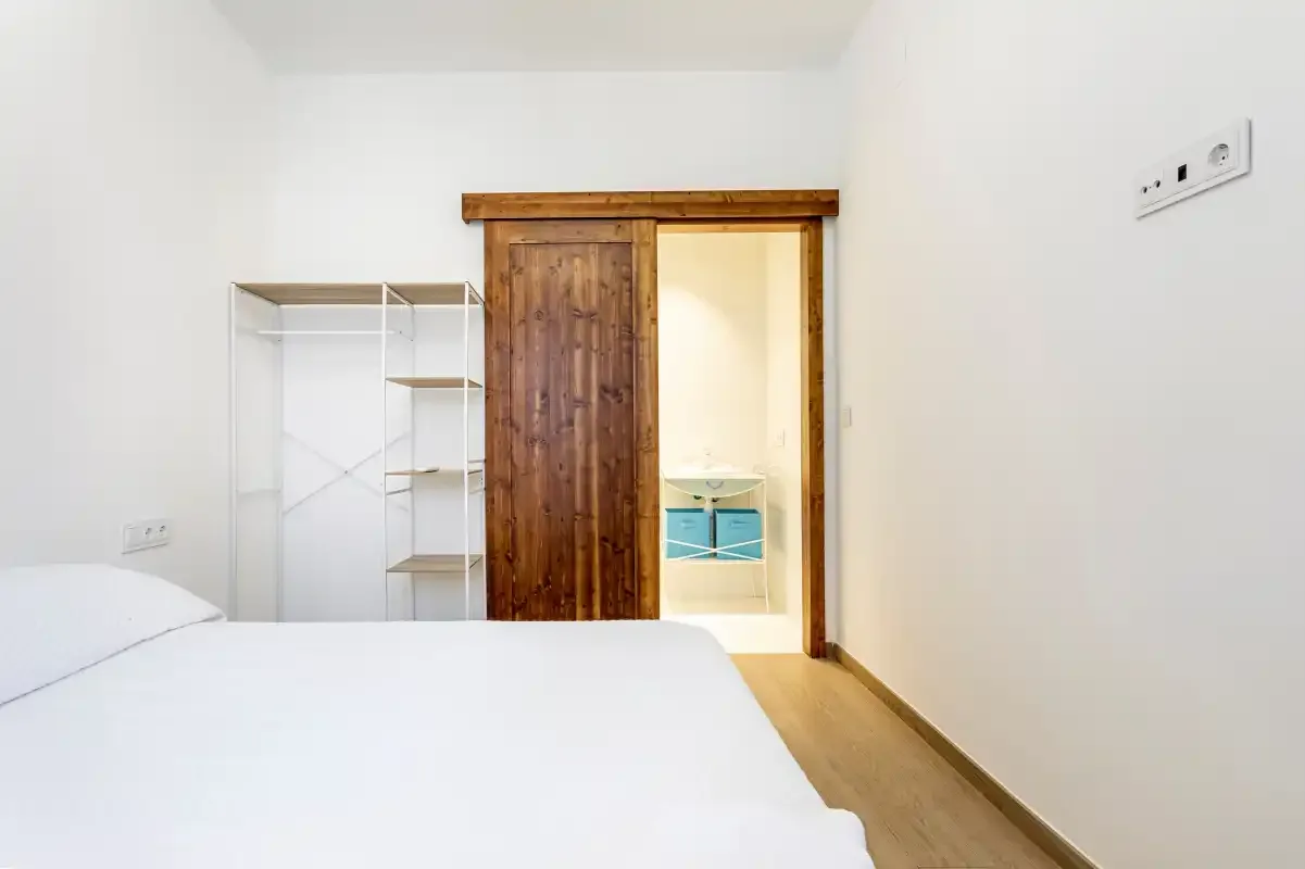 A bedroom with a bed, open shelving, and a wooden sliding door.