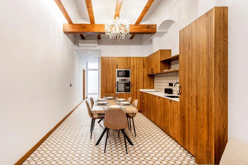 A dining area with a long table beside a wood-paneled kitchen.