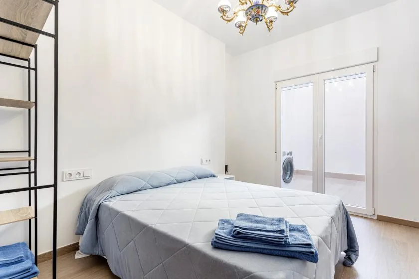 A bright bedroom with a neatly made bed and folded towels.