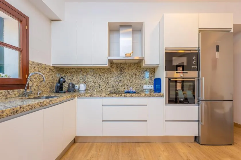 A modern kitchen with white cabinets, stone-patterned counters, and built-in appliances.