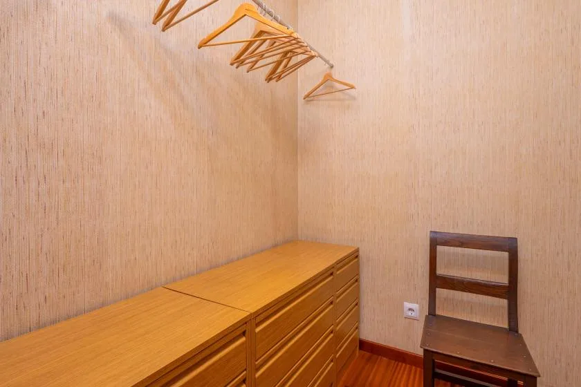 A small dressing area with wooden drawers, hangers, and a chair.