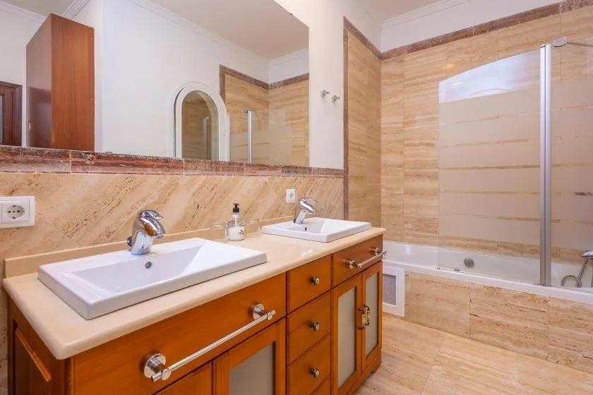 A bathroom vanity with two sinks stands beside a bathtub with a glass screen.