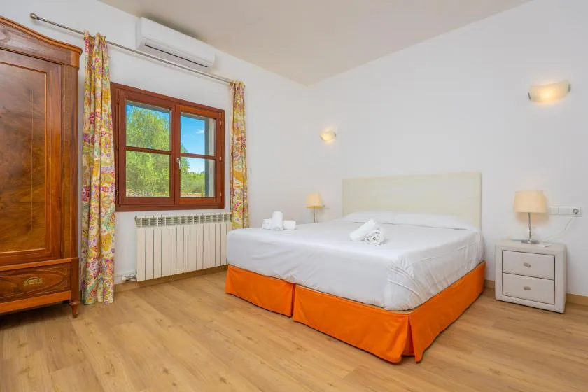 A bright bedroom with a bed, a window, and wooden flooring.
