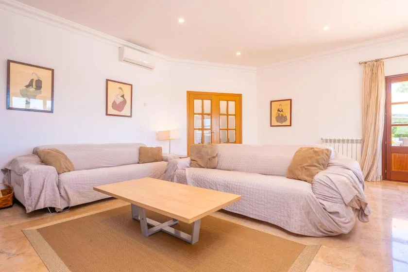 A living room with light-colored seating, a wooden coffee table, and framed wall art.