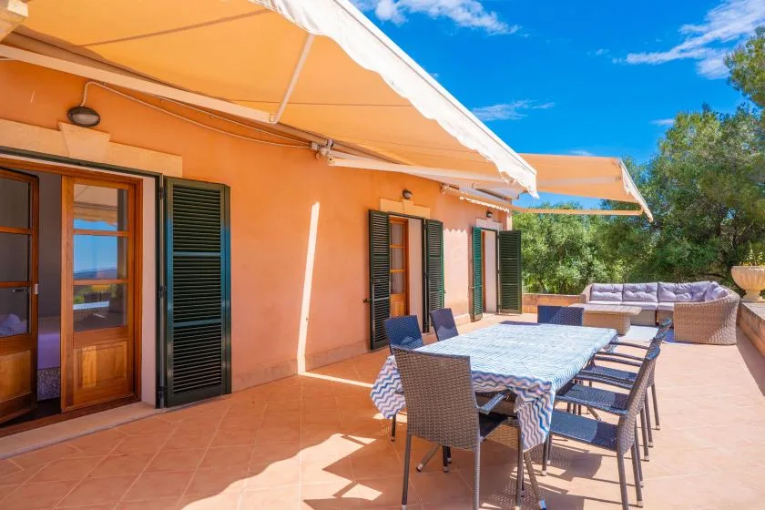 A sunny outdoor dining terrace beside an orange building, with a table under an awning.