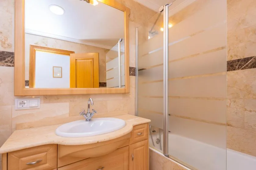A bathroom with a sink vanity, large mirror, and glass shower enclosure.