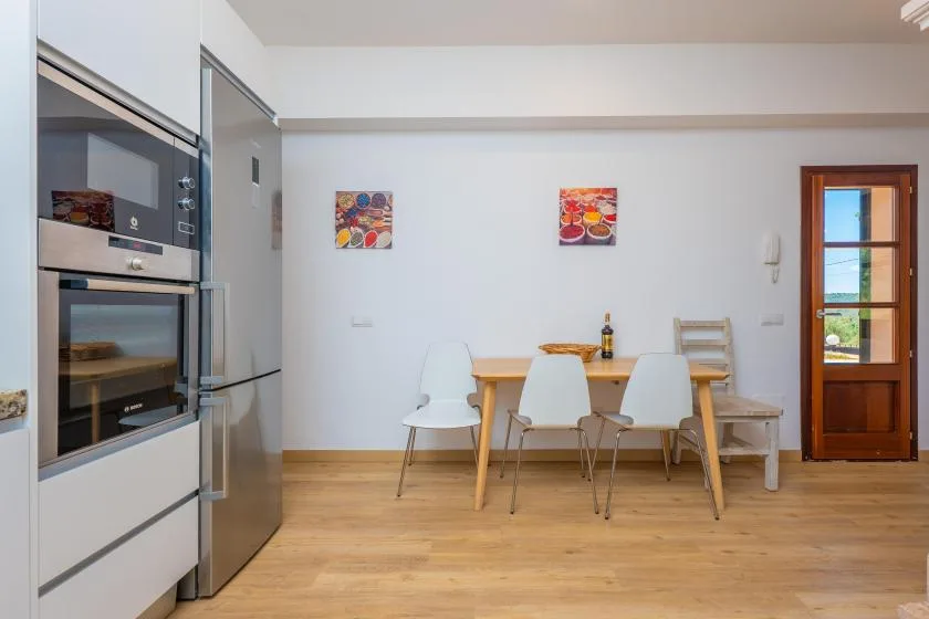 A dining area with a wooden table, white chairs, and two colorful wall pictures.
