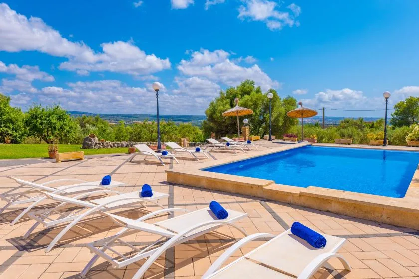 An outdoor swimming pool beside a paved patio with lounge seating and umbrellas.