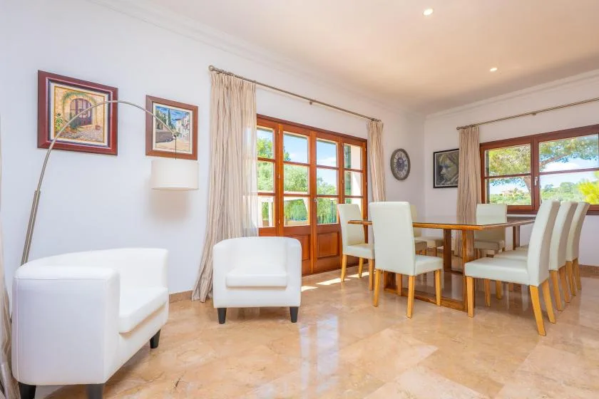 A bright dining area with a wooden table, upholstered seating, and large windows.