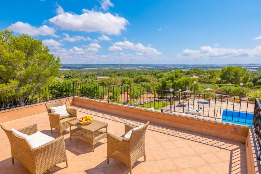 A sunny terrace with outdoor seating overlooks a swimming pool and green landscape.
