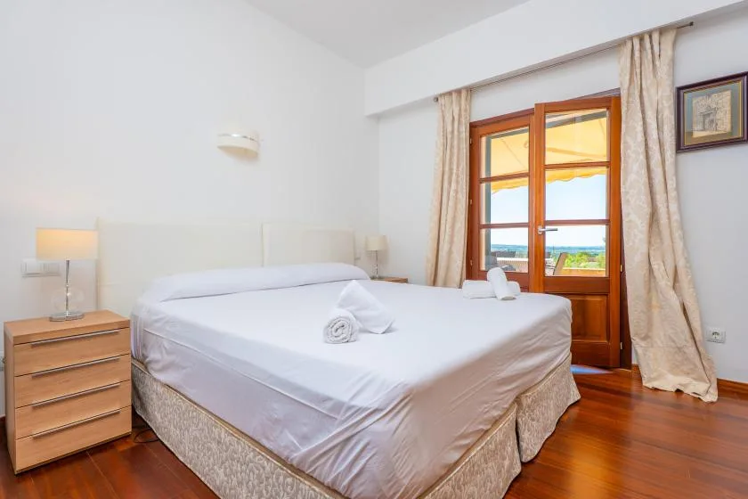 A bedroom with a neatly made bed beside a wooden-framed window.