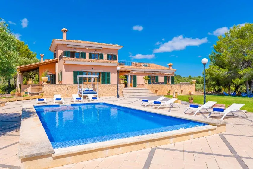 A swimming pool in front of a two-story house, with lounge chairs on the patio.