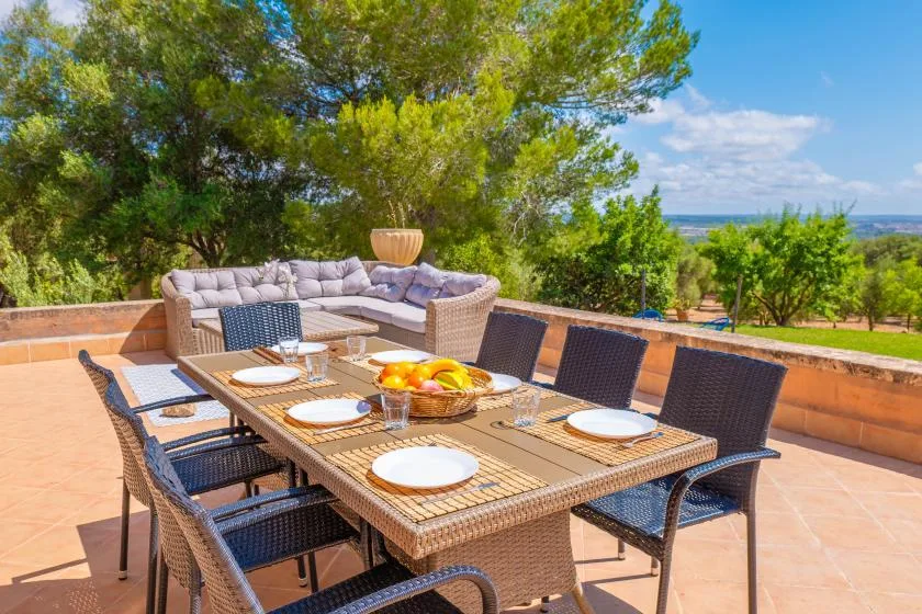 A tiled outdoor dining area with a table and seating beneath leafy trees.