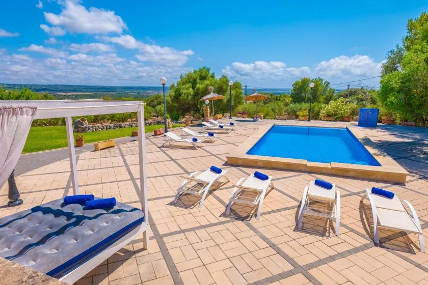 An outdoor pool and surrounding tiled patio with lounge chairs under a sunny sky.