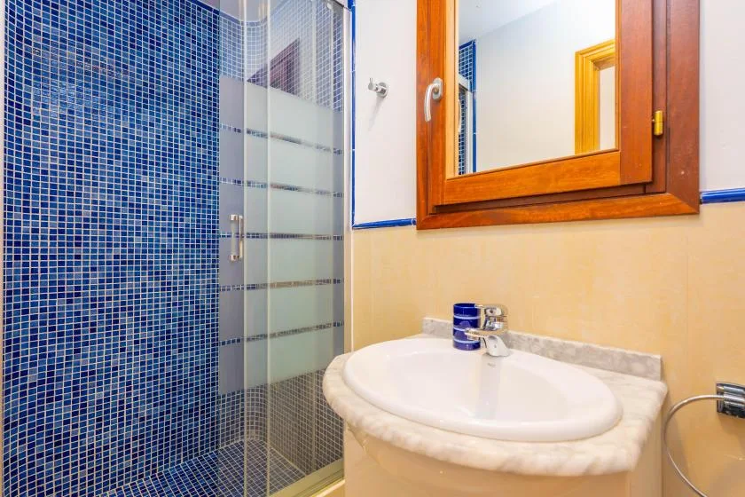 A bathroom with a glass shower and a sink beneath a wooden-framed mirror.