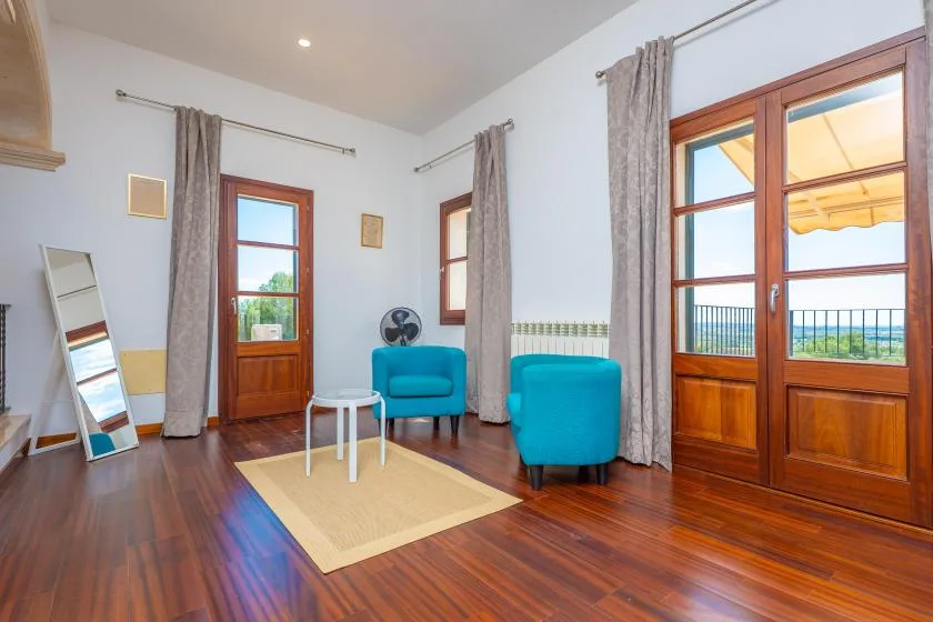 A bright sitting room with turquoise seating, tall windows, and wooden floors.