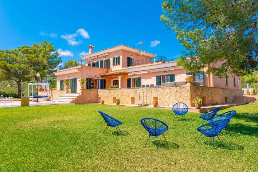 A large house stands behind a grassy yard with several outdoor seats.