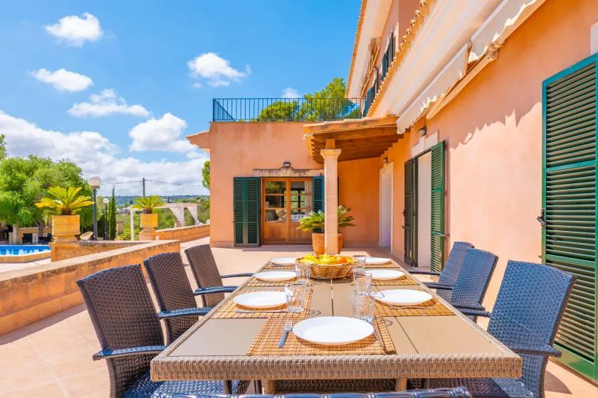 A sunny outdoor dining terrace with a long table and surrounding seating.