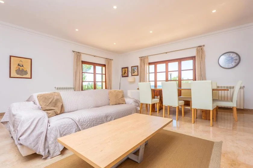 A bright living and dining area with a sofa, table, and large windows.