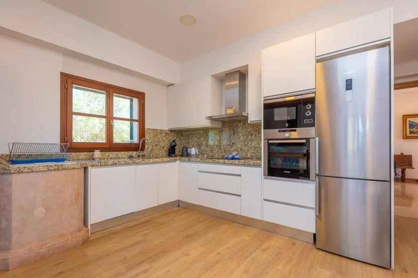 A bright kitchen with white cabinets, a wooden floor, and a window above the counter.