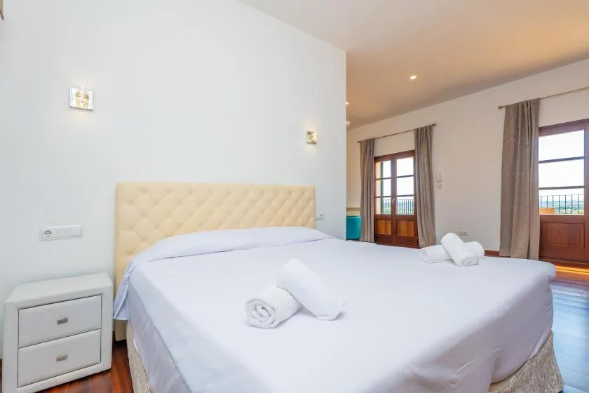 A bedroom with a large bed and tall windows opening onto a balcony.