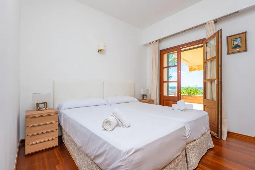 A bright bedroom with two beds and open doors leading to a balcony.
