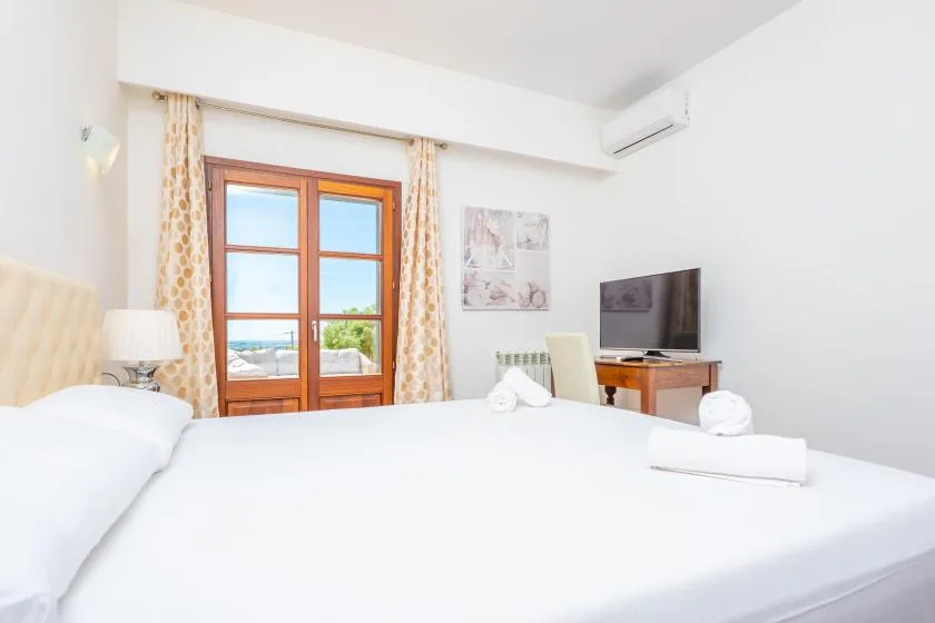 A bright bedroom with a large bed and a television beside the window.