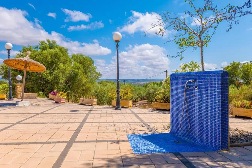 A tiled outdoor patio features a blue shower wall beside a planted garden.