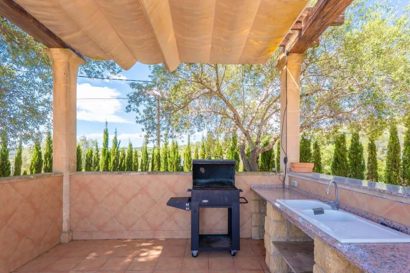 A covered outdoor cooking area has a grill and a counter with a sink.