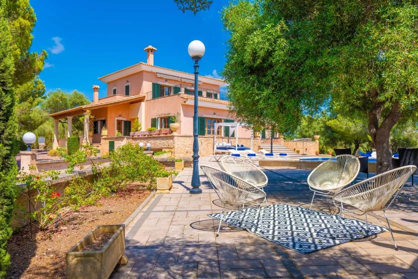 A patio beside a swimming pool, with outdoor seating and a large house in the background.