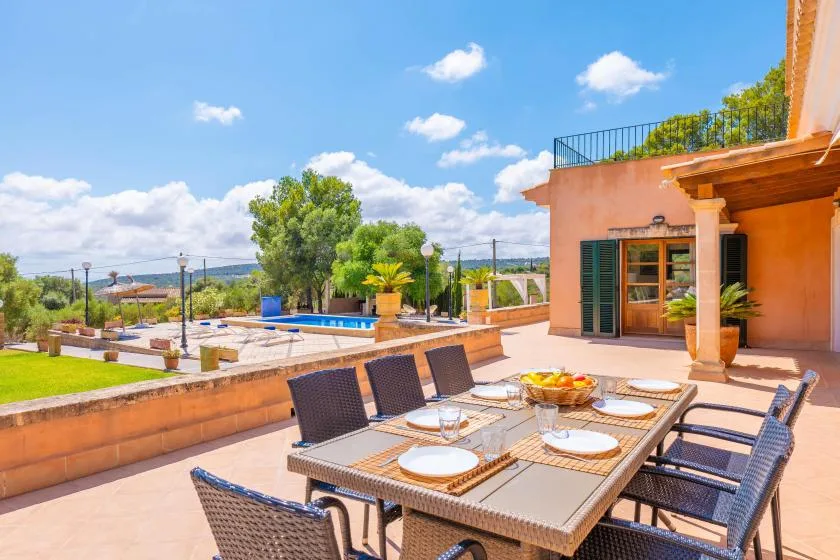 An outdoor dining area overlooks a terrace with a swimming pool and greenery.