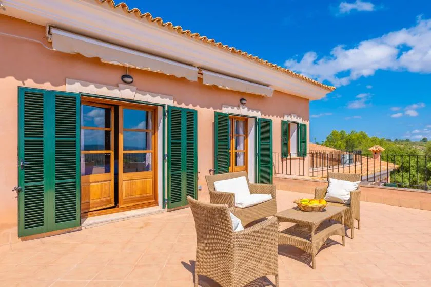 A sunny patio with outdoor seating, green shutters, and views of the countryside.